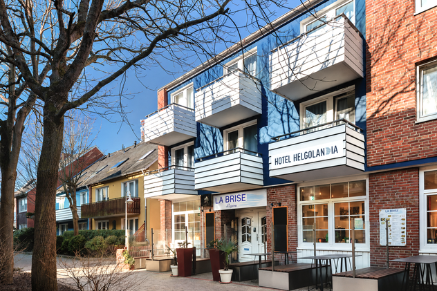Außenansicht des Hotel Helgolandia mit blauer Fassade, weißen Balkonen und dem Bistro La Brise im Erdgeschoss